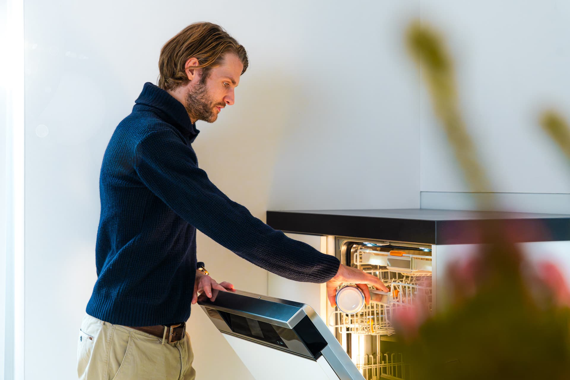 Mies laittaa astioita astianpesukoneeseen modernissa keittiössä, jossa pehmeä valaistus valaisee sisätilaa.