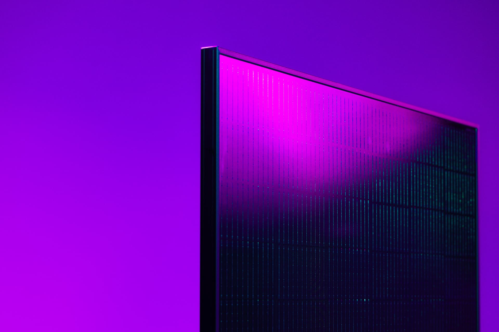 Lähikuva täysin mustan aurinkopaneelin kulmasta eloisan violetin taustan edessä, korostaen sen tyylikästä muotoilua ja ohutta kehystä.