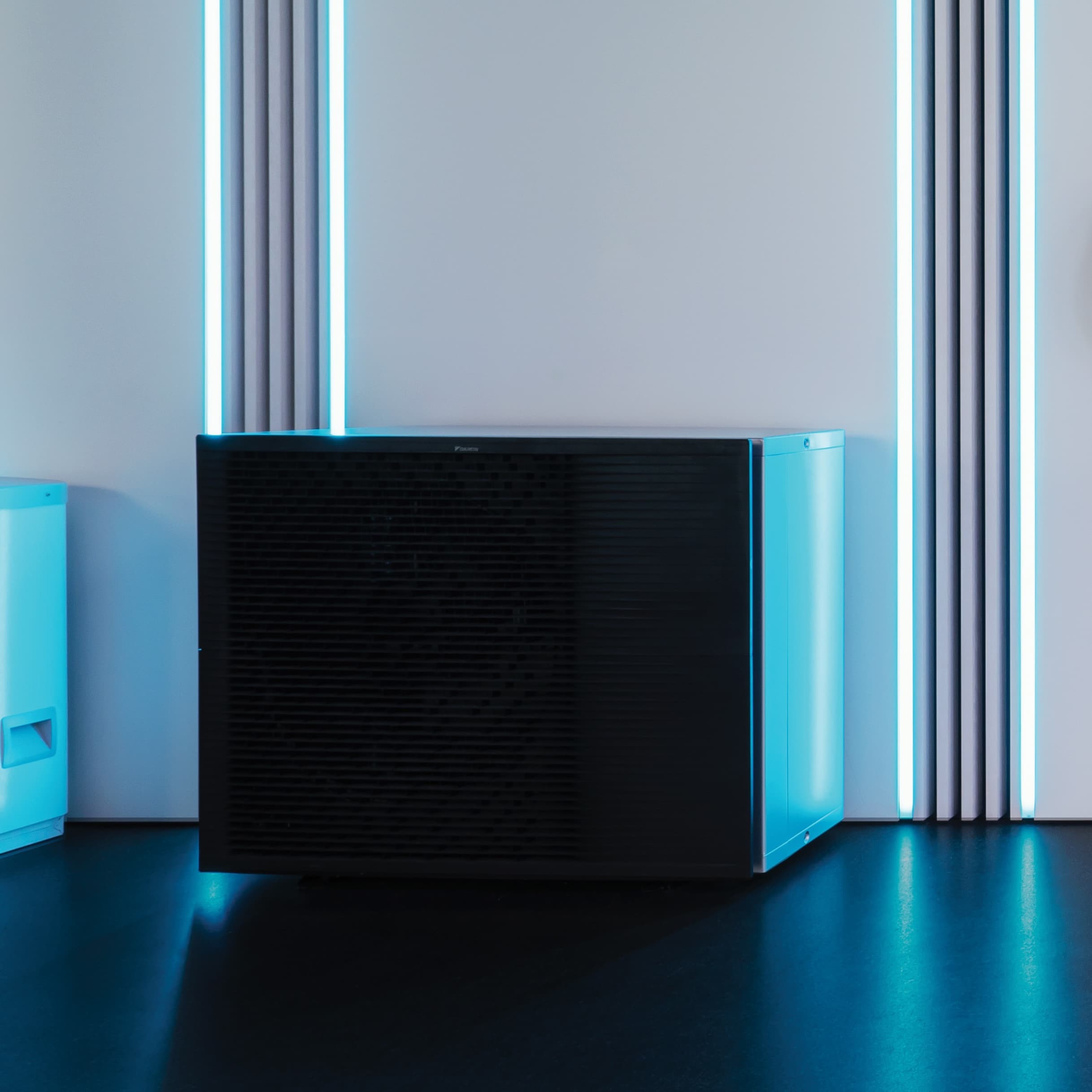 Tyylikäs, moderni musta kuutionmuotoinen lämpöpumppu, jossa on sininen tunnelmavalaistus, minimalistista valkoista seinää vasten.