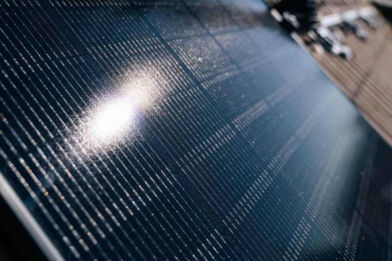 Lähikuva aurinkopaneelista, joka heijastaa auringonvaloa ja paljastaa sen kuvioidun pinnan ja ruutumaista kuviota.