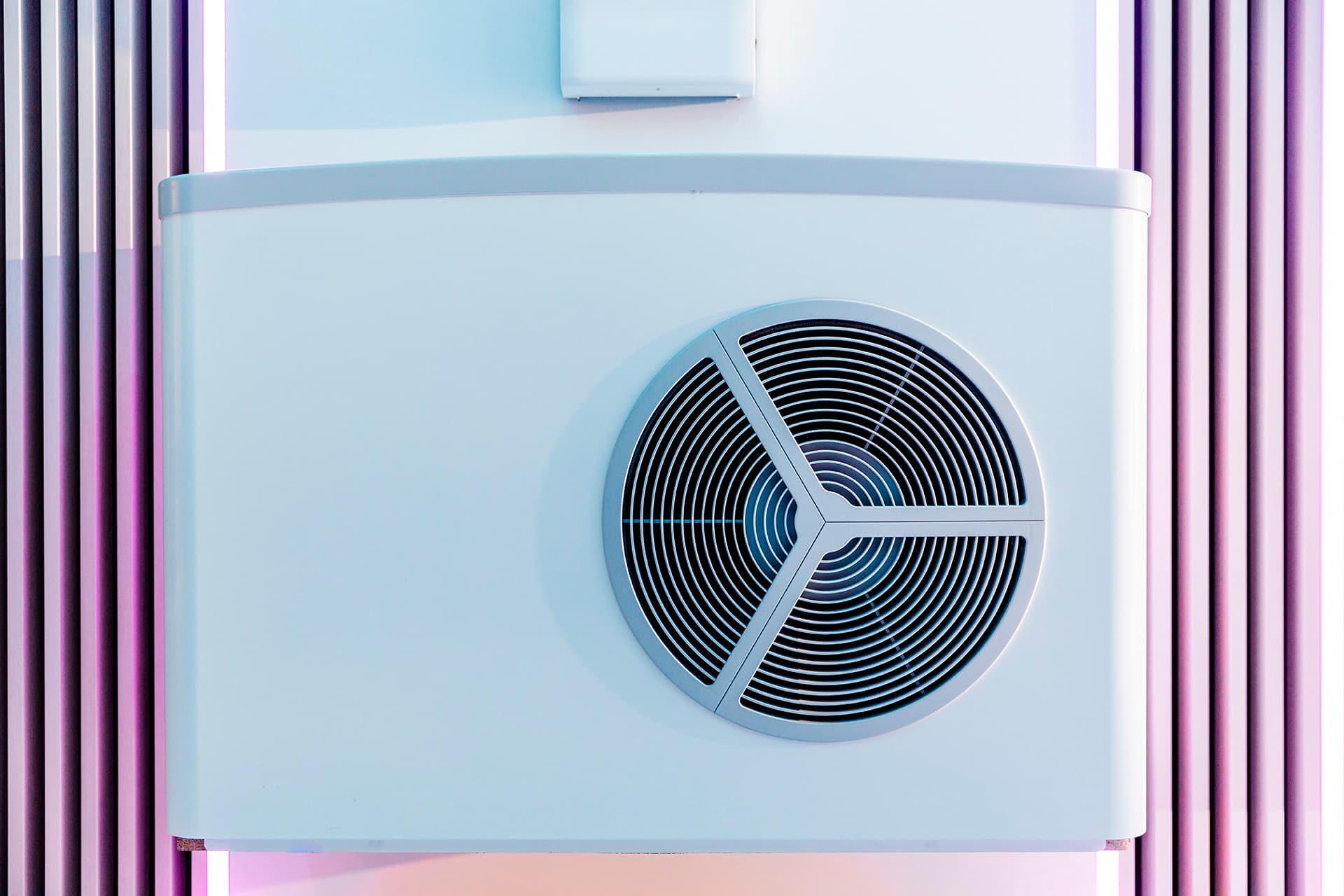 Moderni lämpöpumppuyksikkö, jossa on pyöreä ilmanvaihtoaukko, asennettuna seinälle, jossa on pystysuorat linjat, valaistuna pinkillä ja sinisellä valolla.