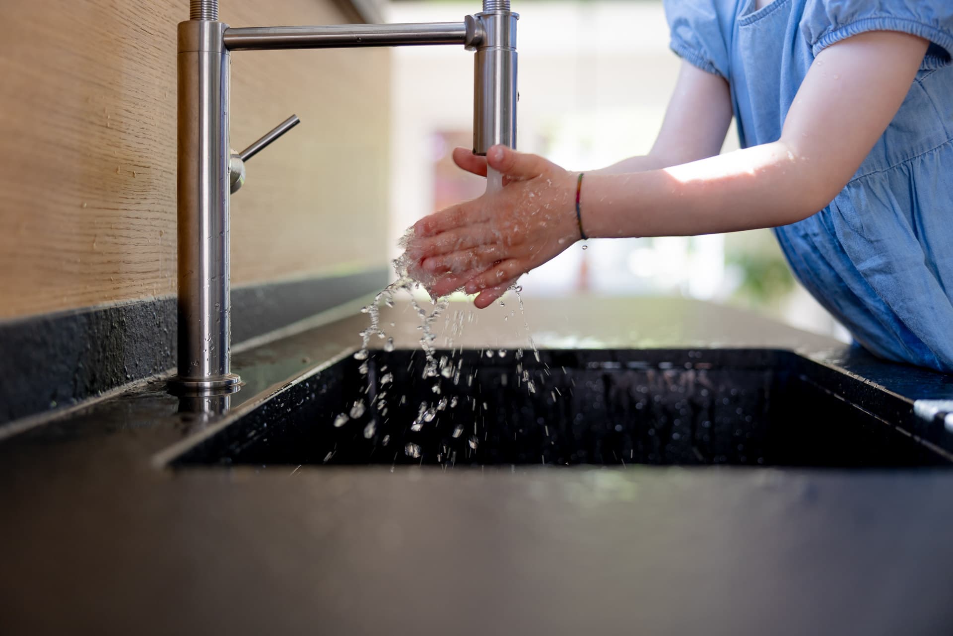 Lapsi pesee käsiään modernin hanan alla keittiön tiskialtaassa, veden roiskuessa.