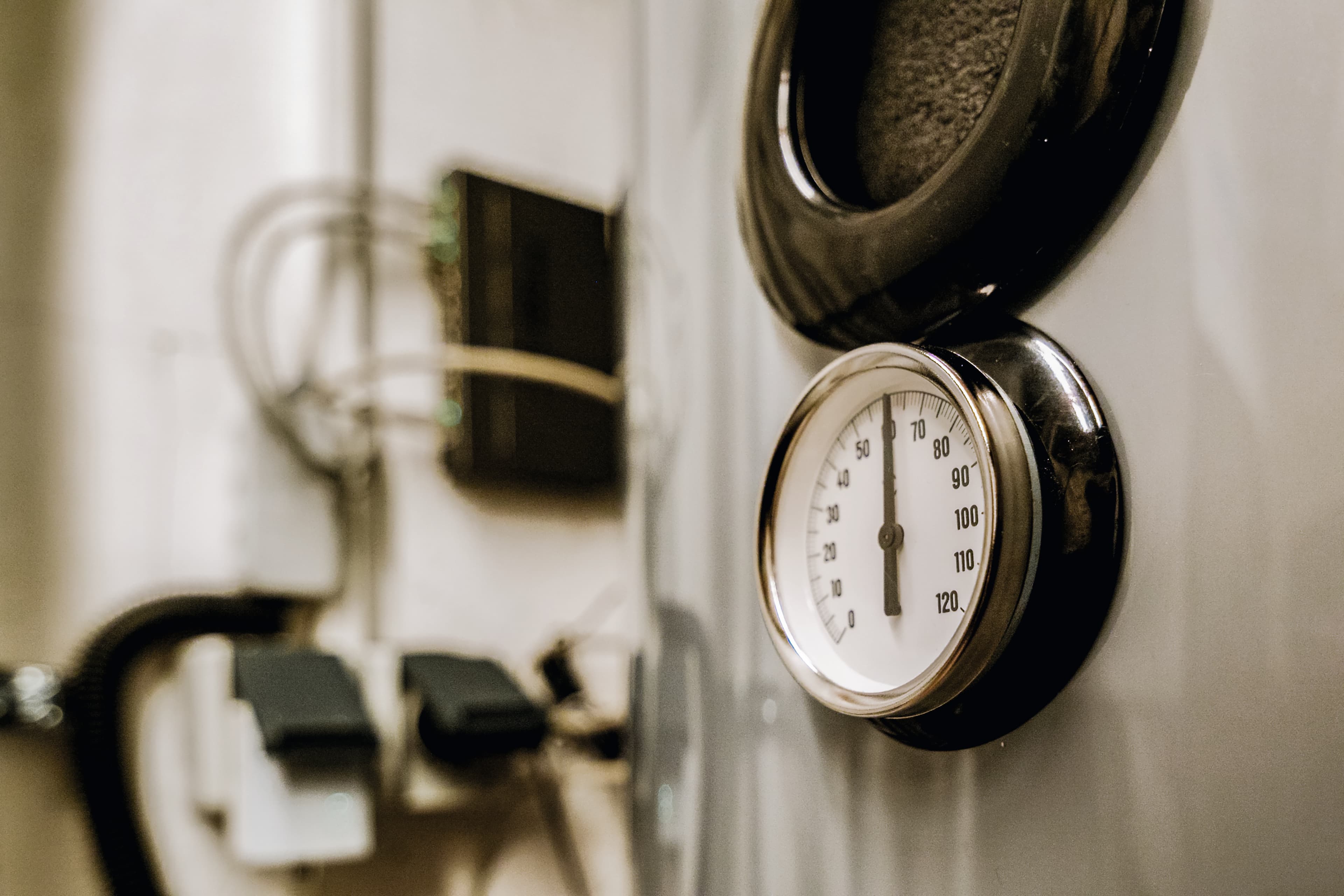 Lähikuva pyöreästä painemittarista teollisuuslaitteessa, asteikko 0:sta 120:een. Taustalla näkyy johtoja ja liittimiä.