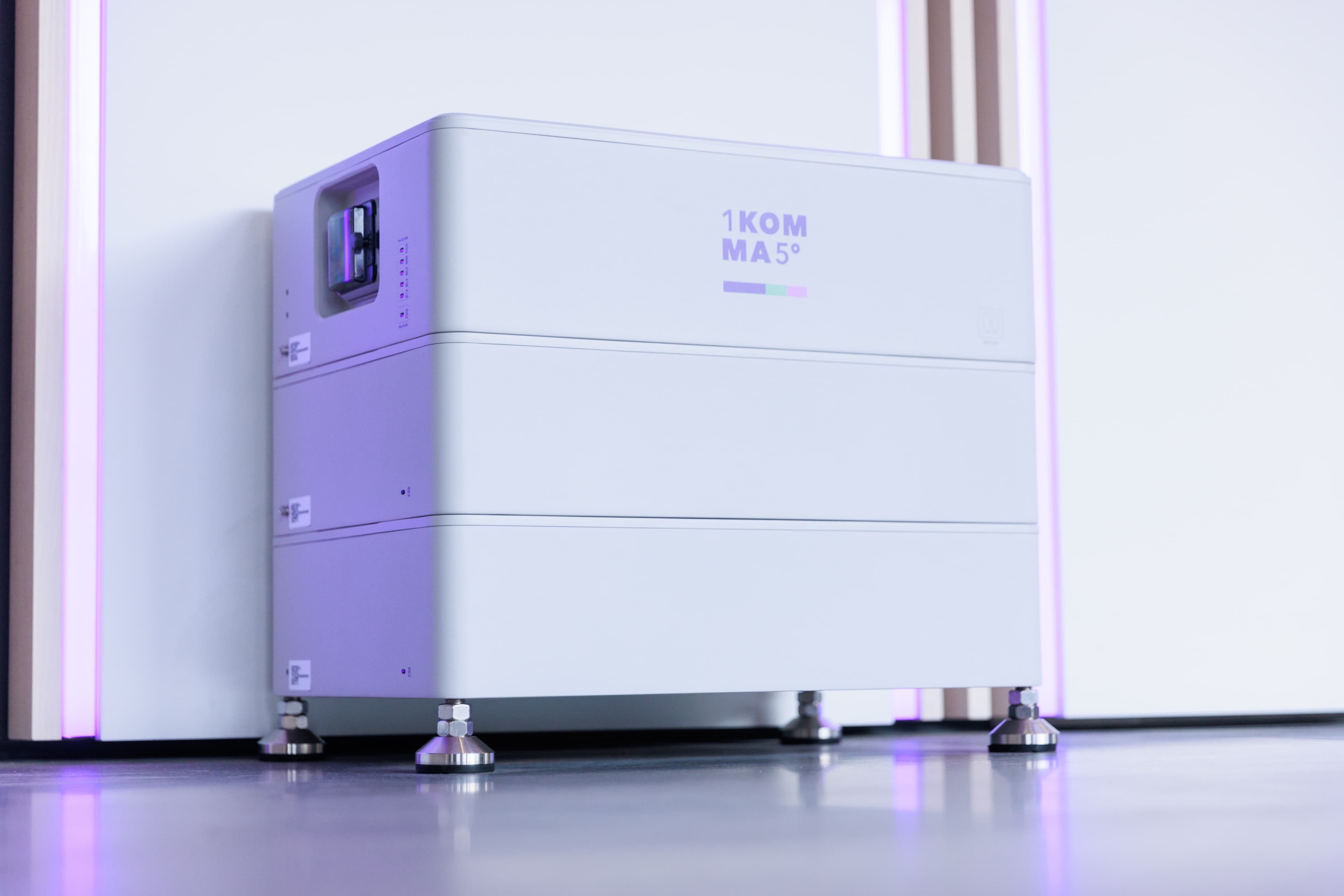 Tyylikäs, moderni virtavarastointilaite, jossa on "1KOMMA5°"-merkintä, on sijoitettu sileälle lattialle säädettävillä jaloilla.